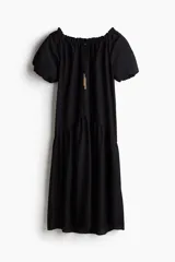 Vestido largo negro con escote cuadrado, cordón ajustable con borlas de cadena, mangas cortas abullonadas con forro y ribete elástico oculto, y costura fruncida bajo la cadera.