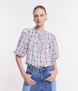Blusa de chiffon con estampado geométrico en tonos blanco, azul y rosa. Tiene cuello redondo con lazo, mangas cortas abullonadas y volados en el cuello y los puños.
