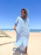 Vestido camisero largo celeste con rayas verticales blancas, cuello camisero, mangas cortas con trabilla y botones, cierre frontal con botones y bolsillos laterales.