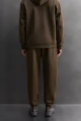 Pantalón jogger de entrenamiento, corte regular fit, color verde oliva oscuro. Confeccionado en tejido técnico compacto de algodón con elasticidad y efecto neopreno. Presenta cintura elástica ajustable con cordón blanco, bolsillos frontales y un bolsillo lateral con cierre de cremallera. El bajo termina en puño.