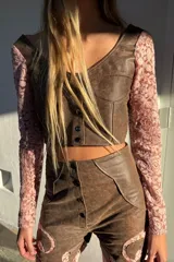 Top confeccionado en cuero color marrón con mangas largas de encaje floral rosado, escote en V y cierre frontal con botones metálicos.