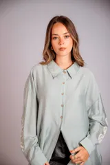 Camisa celeste de corte clásico, con botones frontales y bordados florales en las mangas.