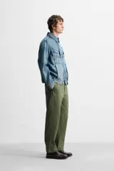 Pantalón chino color verde militar, de corte recto, con bolsillos laterales y traseros de vivo. Cierre frontal con cremallera y botón.