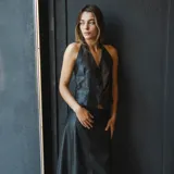 Chaleco negro sin espalda confeccionado en cuero ovino, con cuello halter y cierre frontal con botones.