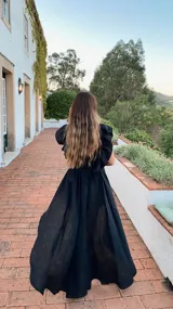 Vestido largo negro de lino, con escote en V, breteles con volados y falda con vuelo. Presenta un corte más corto en la parte delantera y más largo en la parte trasera.