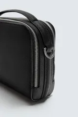 Bandolera negra con textura grabada, compartimento principal con cierre de cremallera, bolsillo interior con cremallera, bolsillo trasero con cremallera y asa de hombro ajustable.