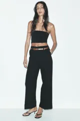 Pantalón marrón de tiro alto con cinturón negro, bolsillos delanteros y cierre frontal con cremallera y gancho metálico.