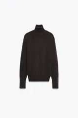 Jersey negro de punto liso con cuello alto, manga larga y detalle de botones dorados en los puños.