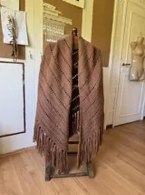 Ruana tejida a mano en color lila, confeccionada en lana merino. Presenta un diseño de punto con calados diagonales y terminación de flecos largos en el ruedo.