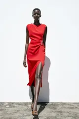 Vestido midi rojo de cuello redondo y sin mangas, con detalle de pliegues y fornitura en la cintura, y abertura frontal en el bajo.