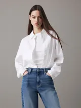 Camisa blanca de algodón Oxford, corte relaxed, cuello en punta, manga larga con puños abotonados y bajo redondeado.