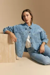 Sobrecamisa de denim celeste con estampado floral tono sobre tono. Presenta cuello camisero, cartera frontal con botones metálicos y bolsillos aplicados en el pecho.