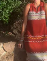 Vestido tejido de punto color ladrillo, sin mangas, con cuello polo y diseño con motivos geométricos en blanco, amarillo y marrón.