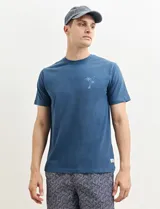 Remera verde con estampado en la espalda de una playa con palmeras y la frase "Ride the waves".