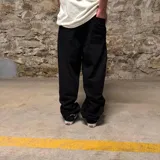 Pantalón de jean negro de corte super baggy con bordados de logos de marcas de automovilismo y texto en blanco y rojo.