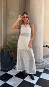 Vestido largo sin mangas, color blanco roto, confeccionado en tejido de red con trama abierta. Se lleva sobre una prenda interior blanca ajustada.