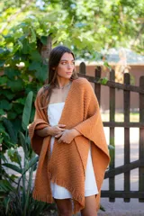 Ruana tejida color ocre con flecos en el borde inferior.