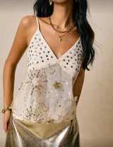 Top blanco con breteles finos, escote en V y apliques de lentejuelas doradas.