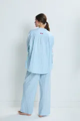 Conjunto de pijama celeste a rayas verticales blancas, compuesto por una camisa de manga larga con cuello mao y botones, y un pantalón de corte recto. La camisa y el pantalón tienen bordados de corazones, soles y otros motivos.