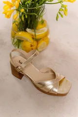 Sandalias doradas de cuero vacuno con tiras cruzadas al frente y cierre con hebilla al tobillo. Taco ancho forrado en madera.