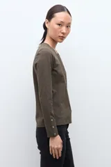 Remera de manga larga color verde oliva, con cuello redondo y botones decorativos en los puños.