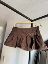 Minifalda negra de jean con tablas, abertura lateral y cinturón con hebilla metálica.