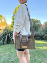 Cartera bandolera de cuero color verde oliva, con forro de tela, bolsillo delantero con cierre y bolsillo interno. Tiene correa larga regulable y manijas cortas.