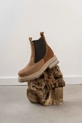 Bota Chelsea color marrón con paneles laterales elásticos negros, suela track color beige y tiradores en la parte superior.
