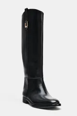 Bota de caña alta color negro, estilo hípico, con punta redonda, suela baja y tira decorativa con hebilla dorada en la caña.