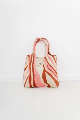 Bolso tejido con diseño estampado a rayas en tonos beige, rosa y marrón. Tiene manijas cortas, cierre con broche a presión y etiqueta de marca.