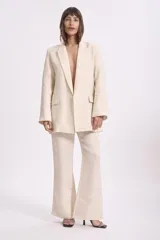 Blazer color crema con textura de lurex, solapas clásicas, corte recto y bolsillos delanteros.