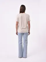 Remera blanca de algodón con cuello redondo y manga corta. Presenta un pequeño bordado en el pecho izquierdo con una figura que parece ser una persona acostada en una tabla de surf o flotador.