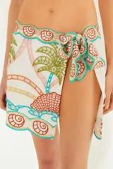 Minifalda playera blanca con bordados de palmeras, olas y conchas en tonos naranja, verde, celeste y amarillo. Tiene lazos laterales para ajustar a la cintura.