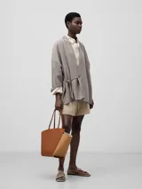 Bolso tipo capazo de cuero color marrón, con doble asa de hombro y cierre lateral con cordones.