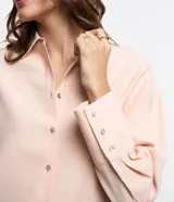 Camisa color rosa pálido, de corte amplio y alargado, confeccionada en viscosa. Tiene cuello camisero, abotonadura frontal y mangas largas con puños abotonados.