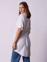 Camisola larga de algodón color blanco, marca Dash. Tiene cuello con solapa, abertura central con botones, bolsillo aplicado en el pecho, mangas regulables con presilla y botón, y bolsillos laterales en la costura.