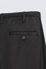 Pantalón negro de corte relajado y pierna ancha, confeccionado en mezcla de algodón y lino. Presenta cintura elástica ajustable con cordón y cierre frontal con cremallera y botón.