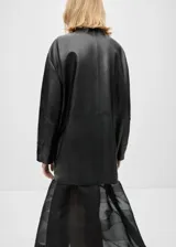 Abrigo negro oversize de cuero ovino con cuello alto y cierre frontal con cremallera y botones ocultos.