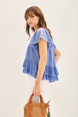 Camisa azul de algodón liviano con cuello redondo y gota en la espalda. Presenta detalle de bordado calado, terminación de volado en mangas y ruedo.