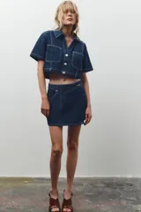 Falda pantalón corta de tiro alto confeccionada en denim azul oscuro. Presenta bolsillos delanteros y traseros de parche. El cierre es cruzado con cremallera oculta y botón metálico.