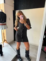 Vestido corto negro con estampado de pequeños lunares blancos. Presenta escote corazón con detalle de botones frontales y volados en las mangas cortas.