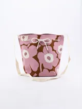 Bandolera tipo bucket de tela tejida con estampado floral en tonos rosa, marrón y blanco. Tiene correa larga de tela color crudo y cierre superior con cordón ajustable.