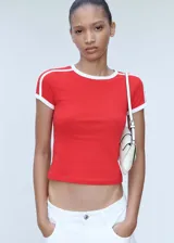 Remera roja de corte recto con cuello redondo y mangas cortas con terminaciones en contraste blanco. Presenta dos líneas blancas paralelas en los hombros.