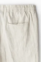 Pantalón de lino liviano para hombre, de corte regular fit y color beige. Presenta cintura elástica con cordón de ajuste oculto, bolsillos laterales discretos y un bolsillo trasero insertado.