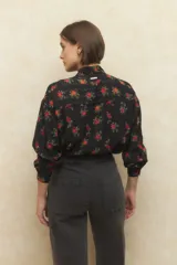 Camisa color crema con estampado de rosas rojas y amarillas, de manga larga y confeccionada en gasa. Tiene cuello con lazo y botones de nácar.