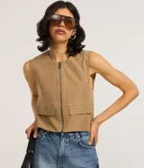 Chaleco color beige de corte sastrero con cierre frontal de cremallera, cuello redondo y bolsillos con solapa.