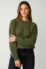 Sweater de poliéster color verde militar, con cuello redondo, manga larga y diseño holgado. Presenta un tejido de punto trenzado con patrones geométricos en el frente.