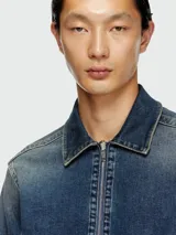 Campera de denim de lavado medio, con cuello camisero y cierre frontal. Presenta detalles de costuras marcadas y parches oscuros en los hombros.