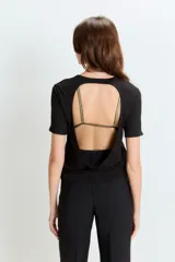Remera negra de mangas cortas con espalda descubierta y tiras doradas de sostén a la vista.