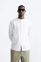 Camisa color beige claro, de corte relaxed fit, confeccionada en tejido de lino y algodón. Tiene cuello mao, manga larga con puños abotonados y cierre frontal con botones.